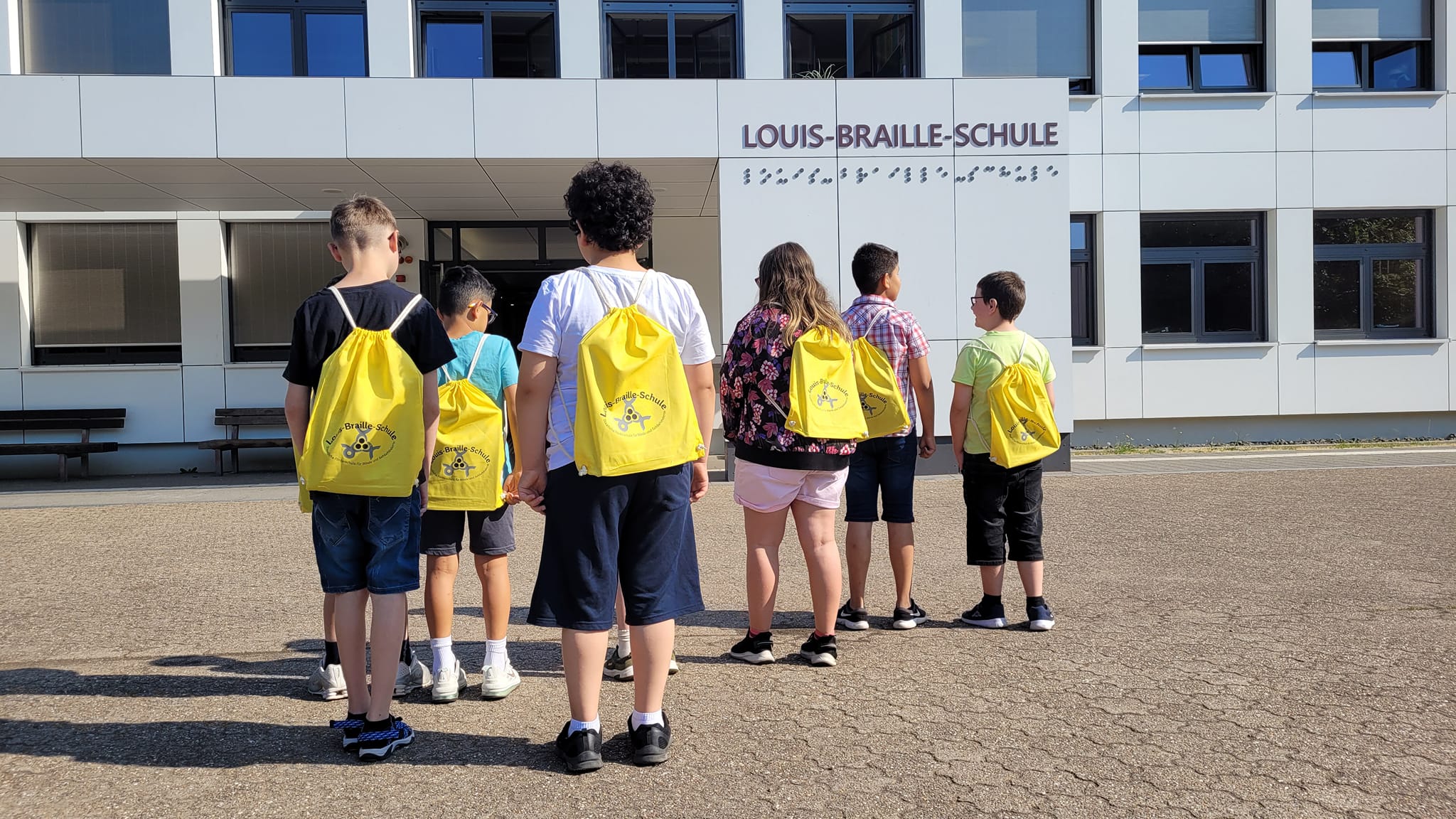 Mehrere%20Sch%C3%BCler%20mit%20Turnbeutel%20vor%20Schulgeb%C3%A4ude